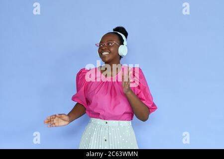 Femme africaine souriante portant des écouteurs et des lunettes de soleil roses dansant sur le lilas. Banque D'Images