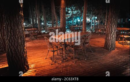 Scène nocturne de la terrasse en bois d'un élégant bar extérieur, éclairé par de petites lampes dans les arbres qui s'élèvent sur la terrasse Banque D'Images