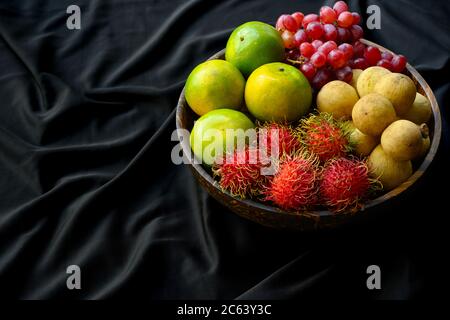 Beaucoup de fruits thaïlandais sont mis ensemble dans un bol en bois sur un tissu noir froissé. Banque D'Images