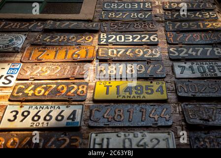 Collage de plaques d'immatriculation pour voitures anciennes, rouillées et grungeuses sur un mur de briques illuminé par des rayons du soleil Banque D'Images