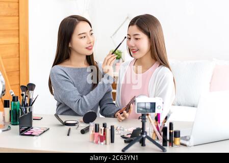 Belle femme asiatique de beauté vlogger faisant la démonstration cosmétique de maquillage avec son ami à la maison Banque D'Images