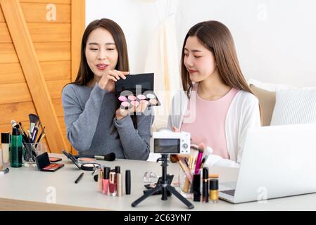 Belle femme asiatique de beauté vlogger faisant examen cosmétique de maquillage avec son ami à la maison Banque D'Images