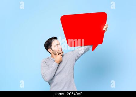 Jeune homme caucasien beau pensant et regardant vers le haut vide rouge bulle de discours isolé sur fond bleu clair Banque D'Images
