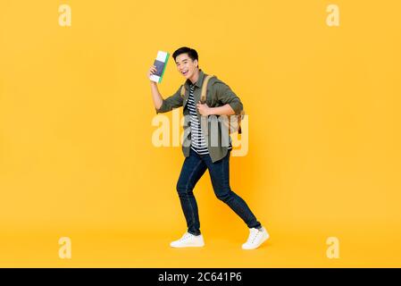 Jeune homme asiatique voyageur seul avec passeport à dos et carte d'embarquement prêt à voler sur fond jaune isolé Banque D'Images