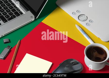 Drapeau national du Bénin sur la vue de dessus espace de travail de créateur avec ordinateur portable, clavier d'ordinateur, clé usb, tablette graphique, tasse de café, souris sur bois Banque D'Images