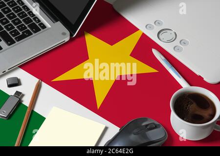 Drapeau national du Suriname sur la vue de dessus espace de travail de créateur avec ordinateur portable, clavier d'ordinateur, clé usb, tablette graphique, tasse de café, souris sur woo Banque D'Images