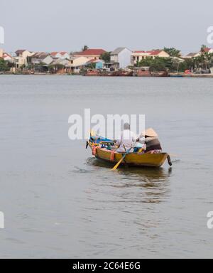 Couple vietnamien local aviron le canoë vietnamien traditionnel sur la puissante rivière Thu bon à la périphérie de Hoi an Vietnam. Banque D'Images