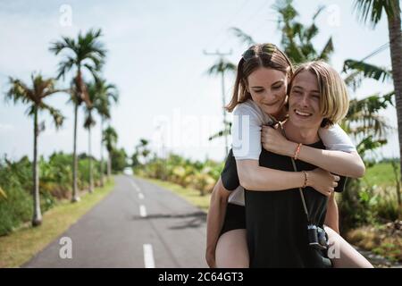 Un homme portant sa petite amie au milieu de la route entouré par une vue exotique tropicale Banque D'Images