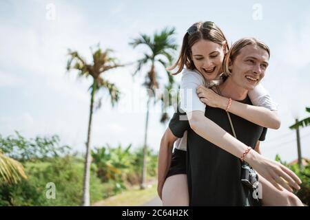 Un homme portant sa petite amie au milieu de la route entouré par une vue exotique tropicale Banque D'Images