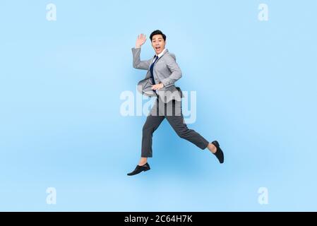 Portrait plein de plaisir de jeune homme d'affaires asiatique écostatique heureux sautant en plein air isolé sur fond bleu studio Banque D'Images