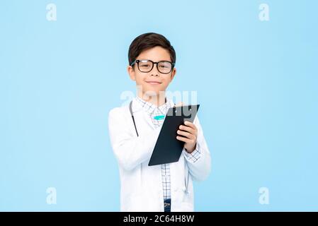 Portrait d'enfant asiatique souriant aspirant à être futur médecin écrivant la prescription dans le presse-papiers dans un fond bleu isolé Banque D'Images