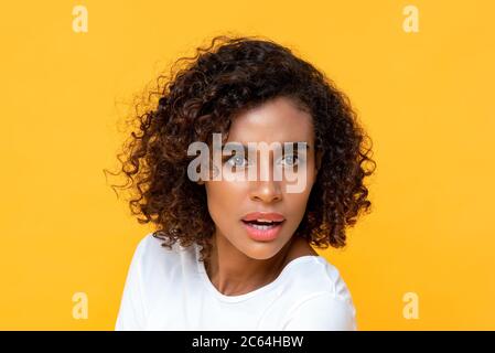 Portrait en gros plan de jeunes curieux et belle femme afro-américaine qui regarde un arrière-plan jaune studio isolé et étonnant Banque D'Images