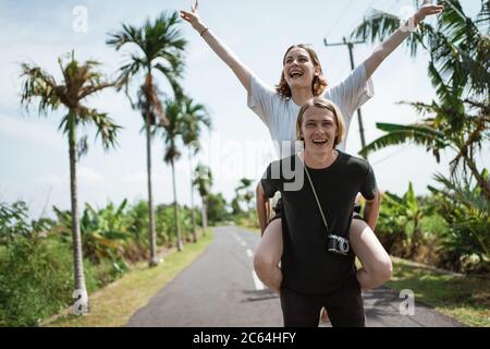 Un homme portant sa petite amie au milieu de la route entouré par une vue exotique tropicale Banque D'Images