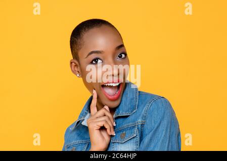 Portrait amusant de jeune femme afro-américaine souriante montrant le doigt sur la joue avec la bouche ouverte sur fond jaune isolé de studio Banque D'Images