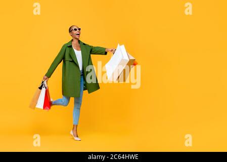 Portrait complet d'une femme afro-américaine attrayante et gaie tenant des sacs de shopping tout en dansant sur fond jaune studio isolé Banque D'Images