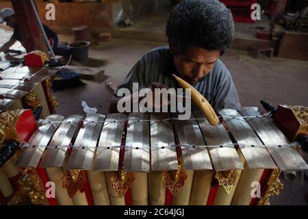 Un travailleur qui teste les sons produits par un gamelan nouvellement construit dans un atelier de gong et de gamelan balinais à Gianyar, Bali. Banque D'Images