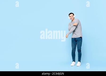 Portrait complet d'un jeune caucasien souriant, portant un casque, écoutant de la musique tout en dansant sur fond bleu isolé Banque D'Images