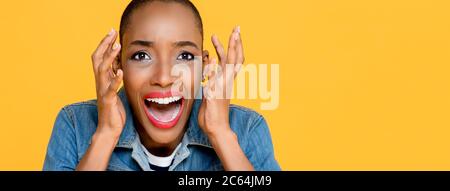 Portrait panoramique de la jeune femme afro-américaine effrayée hurlant des deux mains soulevées isolée sur fond jaune studio Banque D'Images