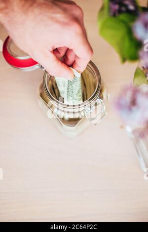 Un homme met des dollars dans un pot de verre pour l'accumulation - une banque de piggy pour le congé après la quarantaine Banque D'Images