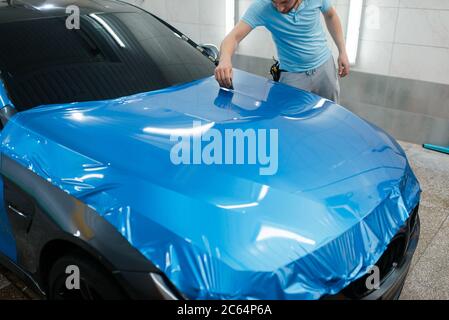 Emballage de voiture, homme avec raclette installe le film Banque D'Images