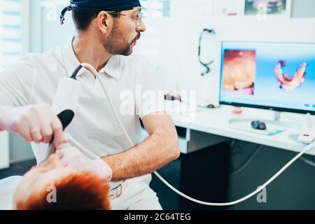 L'orthodontiste du médecin scanne la cavité buccale du patient et contrôle le processus sur le moniteur - modélisation dentaire 3D Banque D'Images