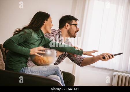 Les jeunes couples regardent la télévision à la maison. Ils font des querelles. Banque D'Images