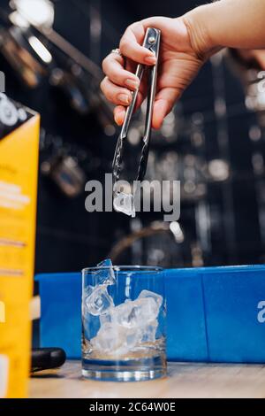 Glace pilée avec des pinces de bar dans un verre pour un cocktail - l'œuvre de Bartender Banque D'Images