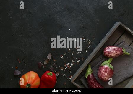 Variétés d'aubergines dans un bol noir sur fond d'ardoise sombre. Vue en hauteur. Banque D'Images