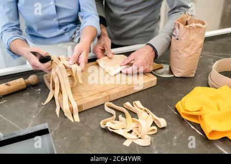 Couple debout dans une cuisine, faisant des pâtes fraîches maison tagliatelle. Banque D'Images