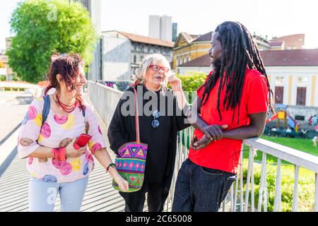 Homme noir avec des dreadlocks et deux femmes caucasiennes debout sur le pont, bavardant et riant. Banque D'Images