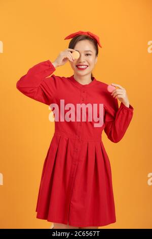 Femme asiatique mignonne en robe rouge tenant macaron sur fond orange. Banque D'Images