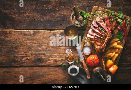 Viande grillée, steak de bœuf en tranches ​​tomahawk aux épices, frites et légumes sur un fond rustique Banque D'Images