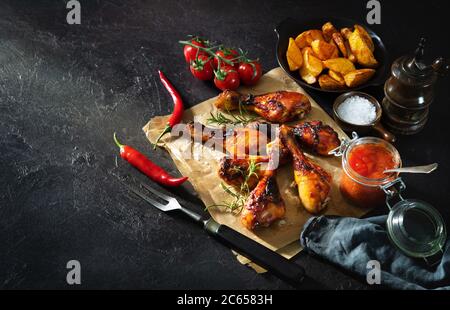 Pilon de poulet grillé servi sur papier avec frites et sauce, vue rapprochée sur table rustique Banque D'Images