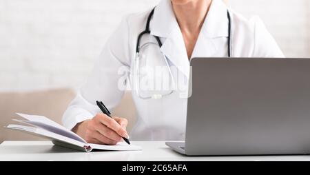 Un patient malade se plaint auprès d'un médecin pour une conférence téléphonique, à l'aide d'un ordinateur portable. Femme en manteau blanc fait des notes dans le carnet Banque D'Images