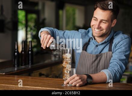 Cocktail du barman. Le barman souriant verse une boisson dans un verre haut avec de la glace Banque D'Images