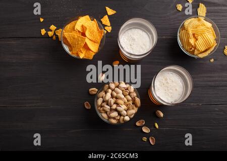 Nachos, chips, pistaches dans des bols en verre et dispersés sur une table en bois, près de sont de la bière avec mousse dans des verres Banque D'Images