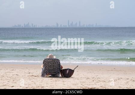 Vue arrière d'une femme assise sur une chaise longue sur la plage de Coolangatta avec la ville de Surfers Paradise en arrière-plan Banque D'Images