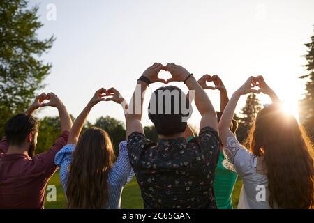 Signe main coeur. Un groupe de personnes tient les mains avec un signe de coeur sur un fond de ciel avec coucher de soleil sur la nature. Banque D'Images