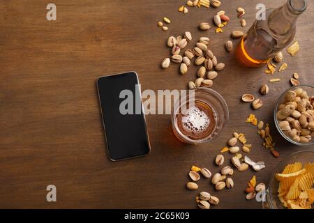 Smartphone sur table en bois, près d'un verre de bière avec mousse, bouteille, noix, copeaux dans des assiettes en verre Banque D'Images