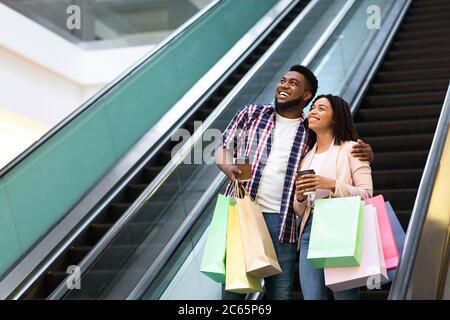 Un bon couple noir qui descend dans l'escalier mécanique après avoir réussi à faire du shopping dans le centre commercial Banque D'Images