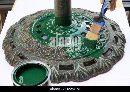 Personne peignant une base circulaire en fonte ornée avec de la peinture verte dans une vue rapprochée sur le pot ouvert de pigments et de pinceau dans un concept de bricolage Banque D'Images