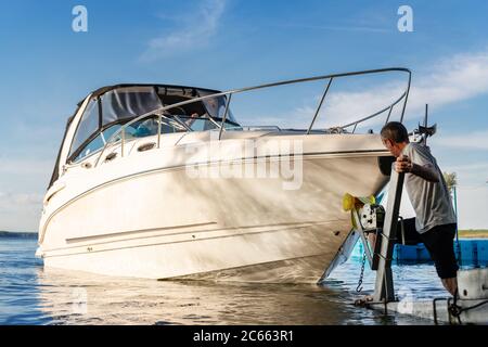 Grand luxe cabine bateau à moteur bateau de croisière yacht lancement à la rampe de remorque sur la rivière ou le lac. Mécanicien homme aide à mettre le bateau dans une surface d'eau calme Banque D'Images