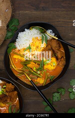 Curry rouge végétarien thaï avec du seitan, des haricots et du chou-fleur sur du riz, servi dans des bols noirs, espace copie Banque D'Images