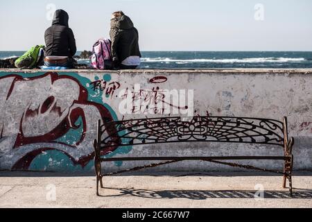 Deux personnes assises sur un mur de quai à Essaouira, surplombant l'océan Atlantique Banque D'Images