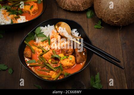 Curry rouge végétarien thaï avec du seitan, des haricots et du chou-fleur sur du riz, servi dans des bols noirs, espace copie Banque D'Images