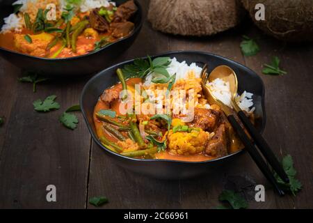 Curry rouge végétarien thaï avec du seitan, des haricots et du chou-fleur sur du riz, servi dans des bols noirs, espace copie Banque D'Images