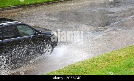 La voiture noire se déplace sur la route sous une forte pluie, de l'eau s'écoule sous les roues. Banque D'Images