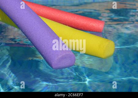 Nouilles de bain aux couleurs vives, pourpres, jaunes et rouges, flottant sur l'eau d'une piscine carrelée de bleu, Banque D'Images