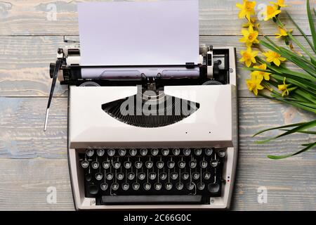 ancienne machine à écrire ancienne vintage avec papier et fleurs jaunes printanières sur fond en bois, joyeuses pâques, femme ou fête des mères, travail de bureau, lettre romantique d'amour, alphabet et clavier Banque D'Images