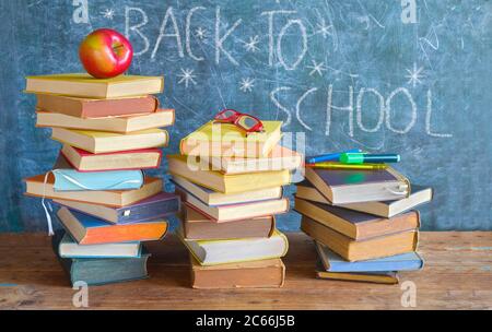 Retour à l'école, piles de livres, pomme, spécifications et fournitures scolaires devant un tableau noir Banque D'Images